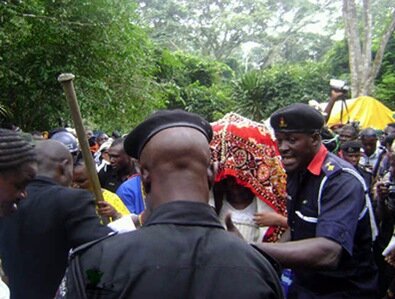 Arugba carrying the calabash of sacrifice, covered with a big red robe at the grove